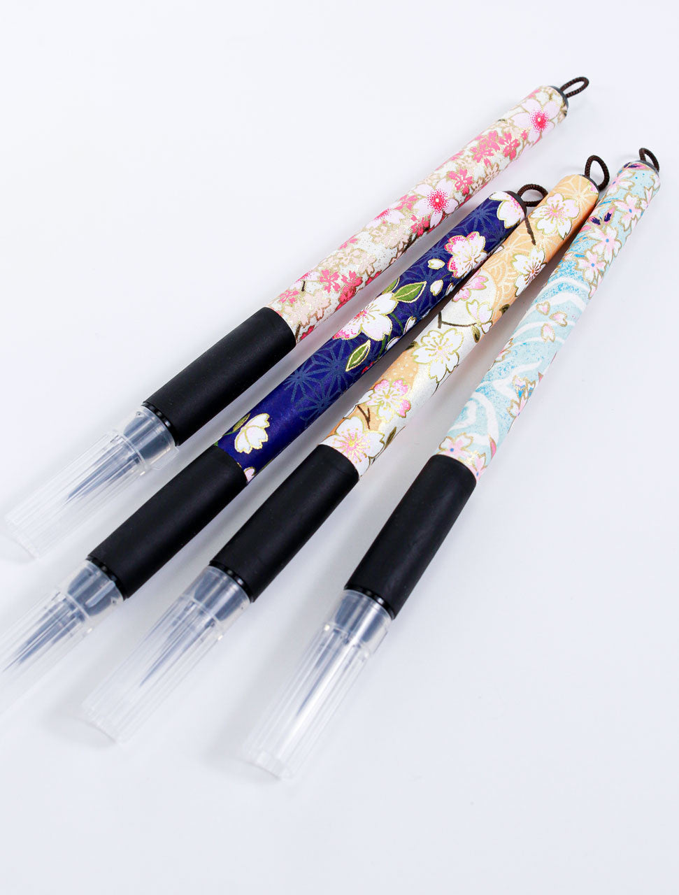 Assorted Sakura fine brush pens wrapped in decorative Japanese Chiyogami paper with black rubber grips and capped felt tips.