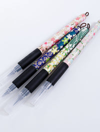 Assorted Sakura fine brush pens wrapped in decorative Japanese Chiyogami paper with black rubber grips and capped felt tips.
