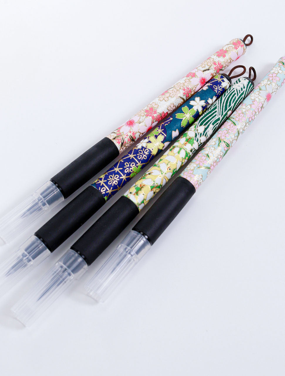 Assorted Sakura fine brush pens wrapped in decorative Japanese Chiyogami paper with black rubber grips and capped felt tips.
