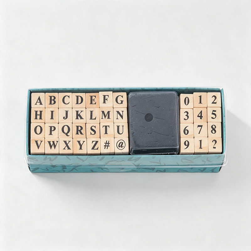 A wooden alphabet and number block set in a teal box, with a black square eraser in the center, photographed from above on a white background.
