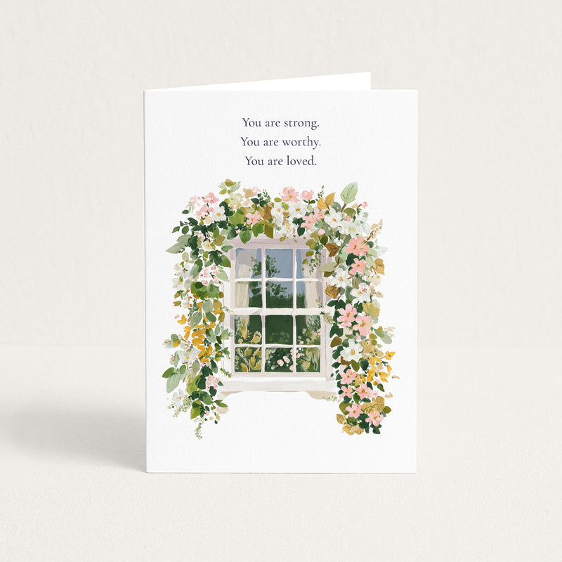 A white greeting card standing upright against a light beige background. The card features the printed message 'You are strong.